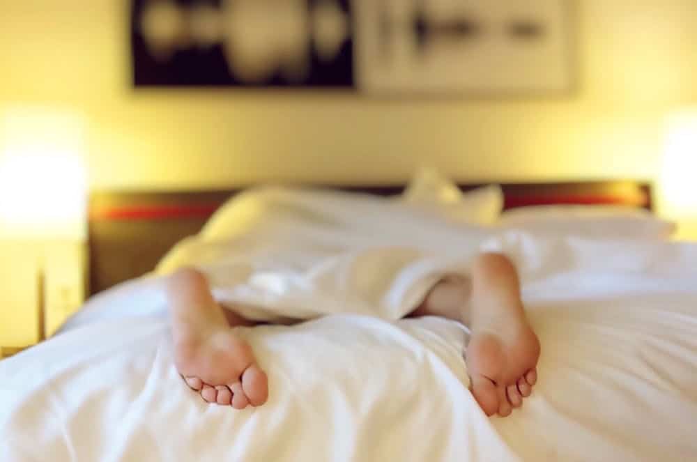 person sleeping on bed with feet outside the blanket