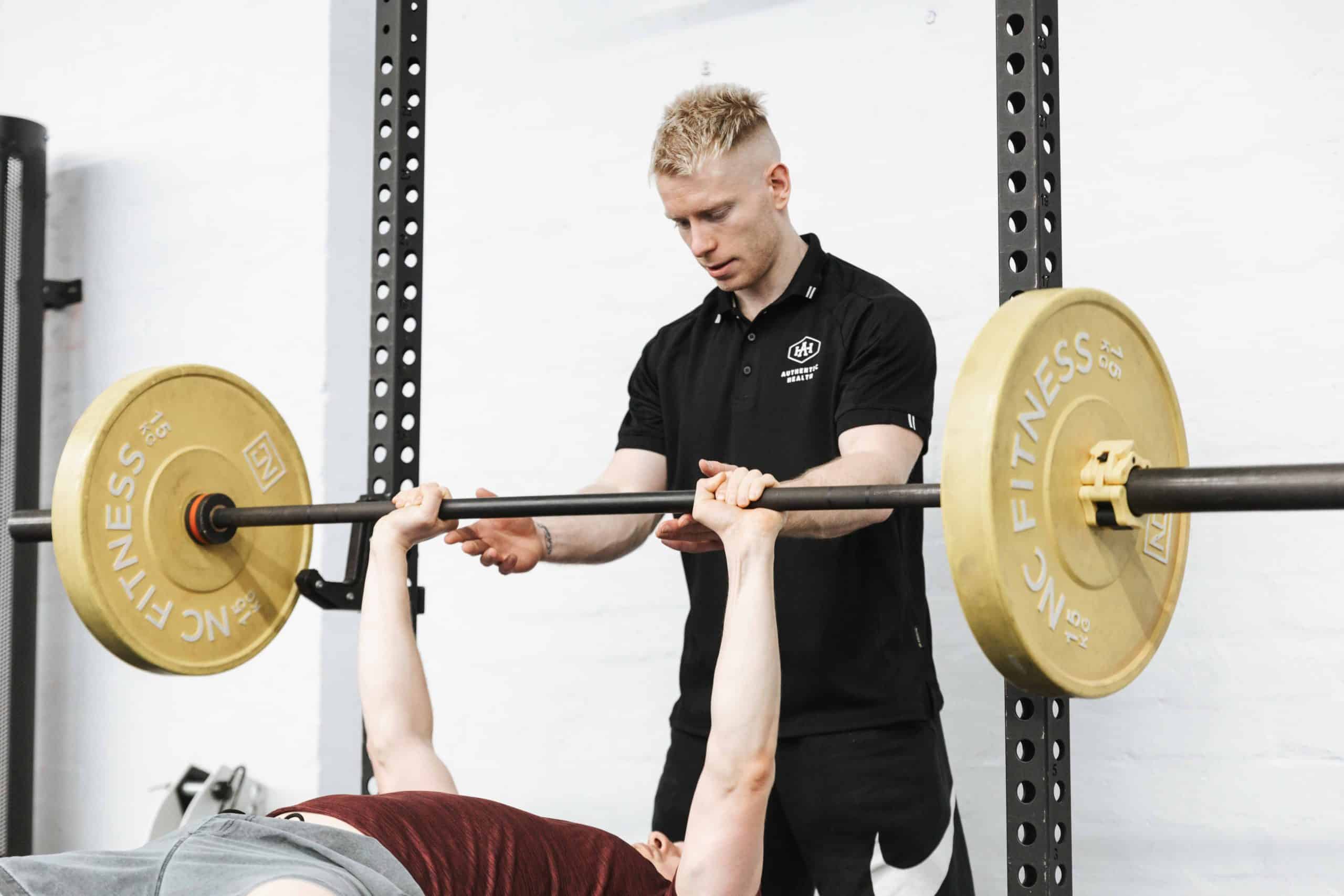 Personal trainer spotting a client's barbell bench press during strength training in Essendon.