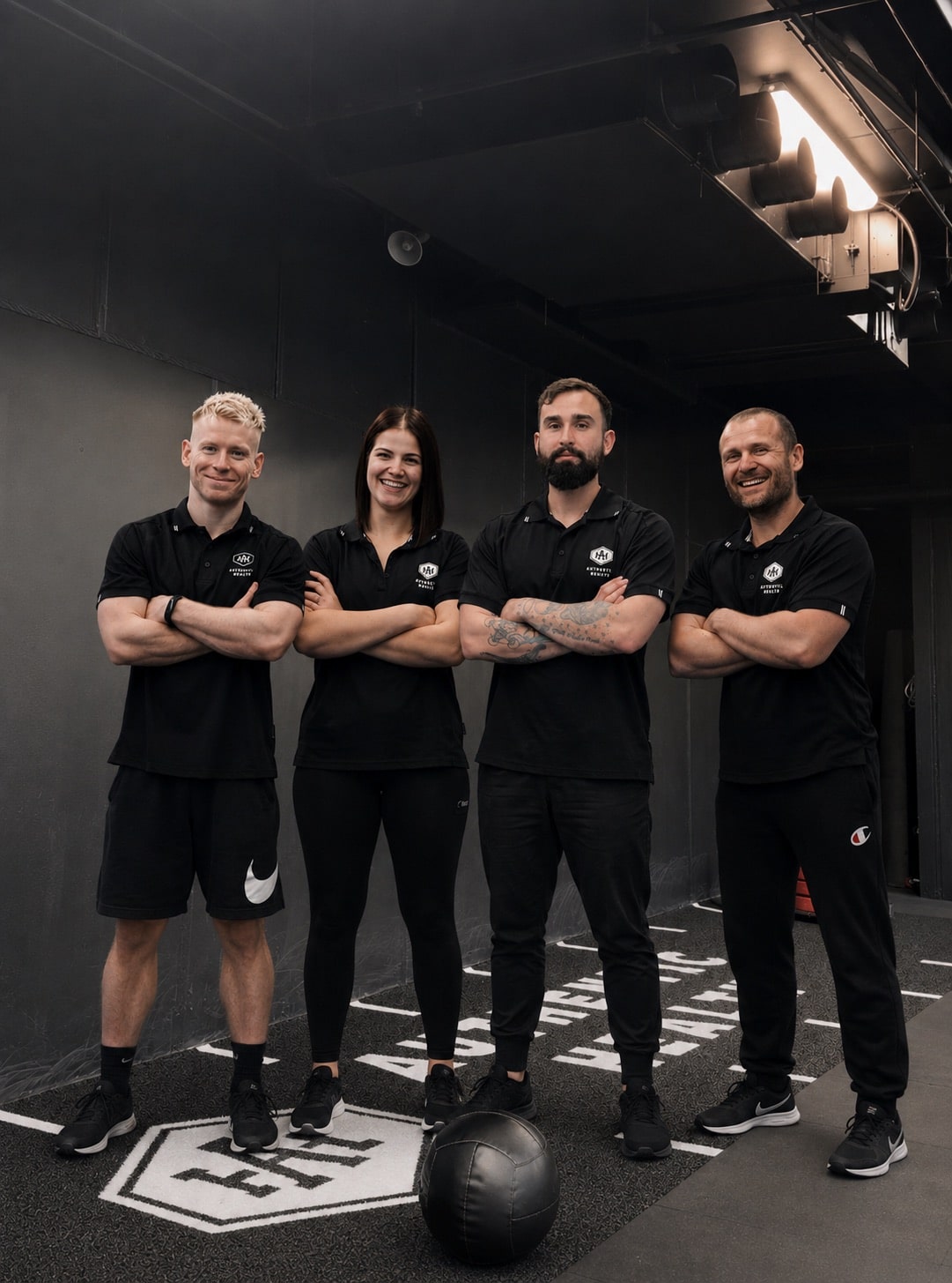 Four Authentic Health Studio personal trainers standing arms crossed in branded black uniforms inside the Essendon studio.