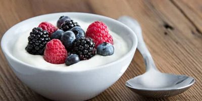 Bowl of fresh mixed berries and yogurt with farm fresh strawberries, blackberries and blueberries served on a wooden table