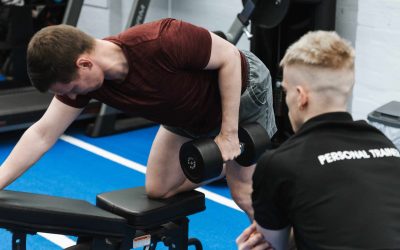 Personal trainer closely watching a client's form during a single arm dumbbell row on a bench.